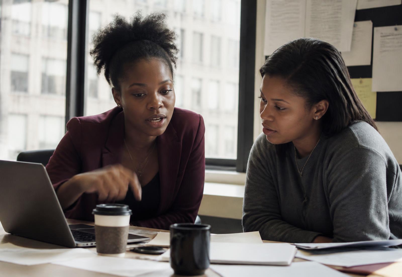 A CueWorks manager coaching a team member over a laptop at a New York office desk